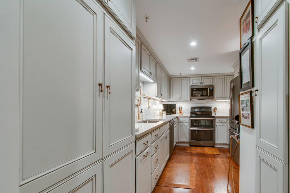 Inspiration for a mid-sized traditional galley separate kitchen in Nashville with an undermount sink, recessed-panel cabinets, grey cabinets, quartz benchtops, white splashback, subway tile splashback, stainless steel appliances, medium hardwood floors, no island, brown floor and grey benchtop.