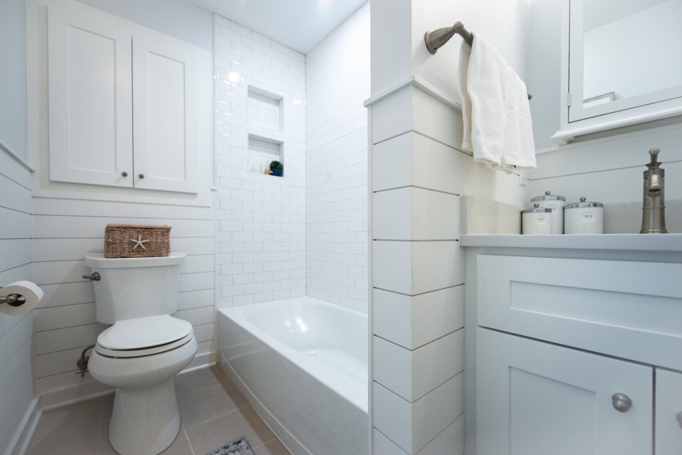 Photo of a small beach style master bathroom in Philadelphia with shaker cabinets, white cabinets, an alcove tub, a shower/bathtub combo, a two-piece toilet, gray tile, stone tile, ceramic floors, an undermount sink, engineered quartz benchtops, a shower curtain, white benchtops, a niche, a single vanity, a built-in vanity and planked wall panelling.