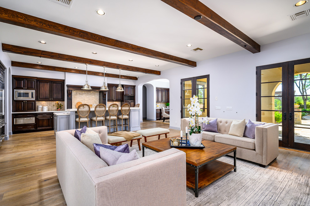 Photo of a large transitional open concept family room in Phoenix with grey walls, light hardwood floors, a standard fireplace, a concrete fireplace surround, a wall-mounted tv and exposed beam.