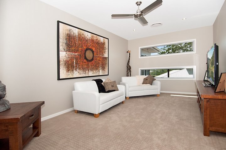Mid-sized asian enclosed home theatre in Sunshine Coast with beige walls, carpet and a wall-mounted tv.