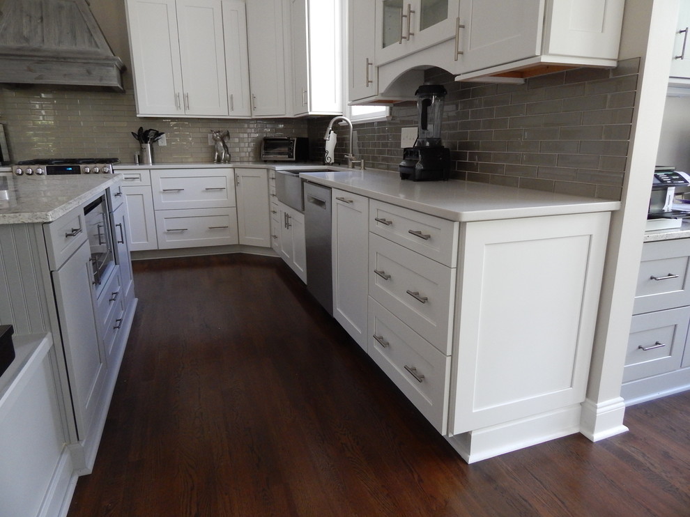 Large traditional l-shaped eat-in kitchen in Charlotte with a farmhouse sink, shaker cabinets, white cabinets, granite benchtops, grey splashback, glass tile splashback, stainless steel appliances, dark hardwood floors and with island.