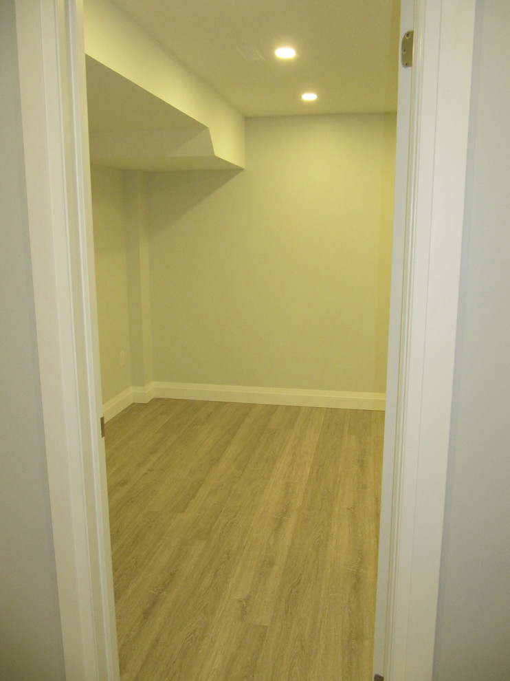 Large modern fully buried basement in Toronto with grey walls, laminate floors, a standard fireplace, a tile fireplace surround and grey floor.