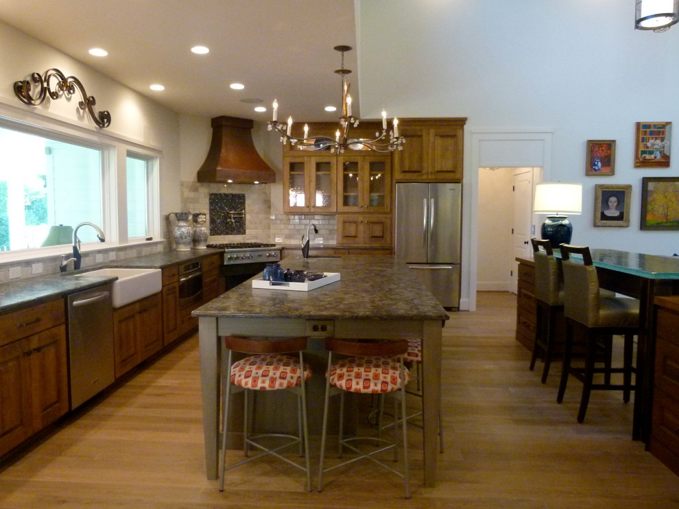 Open concept kitchen - large transitional l-shaped light wood floor open concept kitchen idea with a farmhouse sink, raised-panel cabinets, medium tone wood cabinets, granite countertops, beige backsplash, stone tile backsplash, stainless steel appliances, white walls and two islands