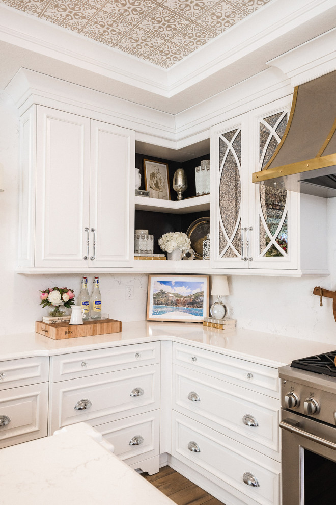 This is an example of a mid-sized traditional u-shaped eat-in kitchen in Other with a farmhouse sink, white cabinets, solid surface benchtops, white splashback, engineered quartz splashback, stainless steel appliances, laminate floors, with island, brown floor, white benchtop and coffered.