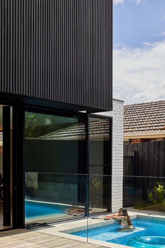 Medium sized and black modern two floor detached house in Melbourne with wood cladding and a metal roof.