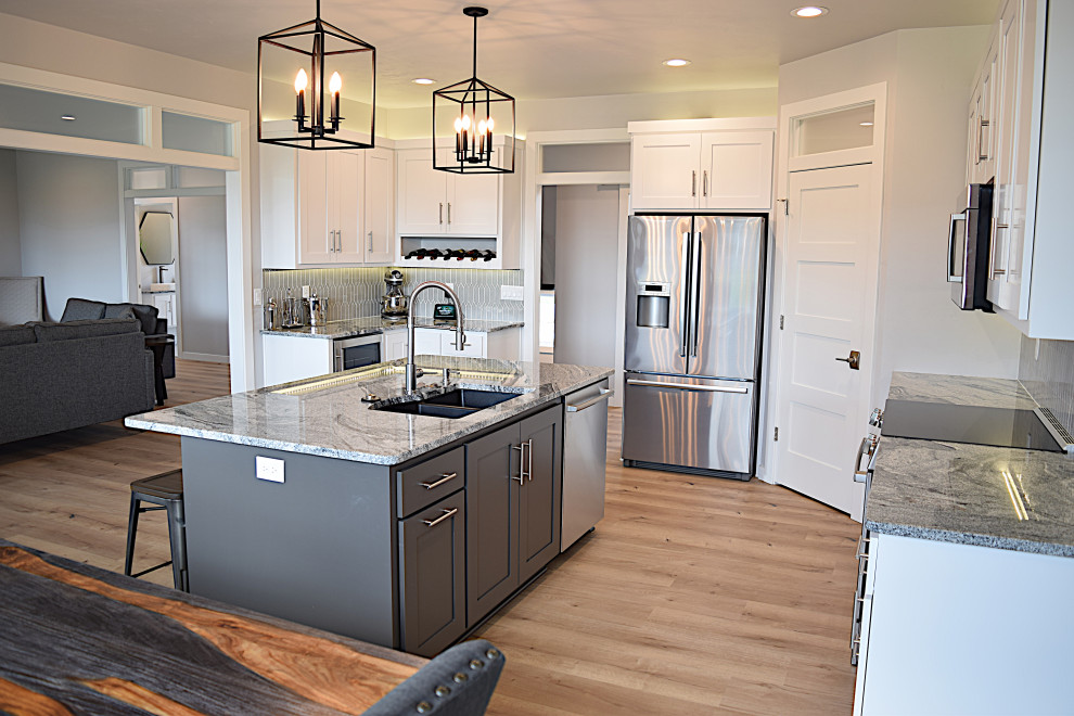 Inspiration for a large light wood floor eat-in kitchen remodel with an undermount sink, recessed-panel cabinets, white cabinets, granite countertops, gray backsplash, ceramic backsplash, stainless steel appliances, an island and multicolored countertops