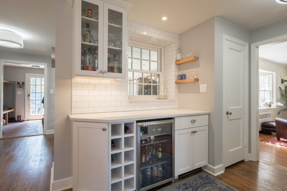 Photo of a large country galley kitchen in Other with a farmhouse sink, shaker cabinets, white cabinets, granite benchtops, white splashback, porcelain splashback, stainless steel appliances, medium hardwood floors, with island, brown floor and white benchtop.