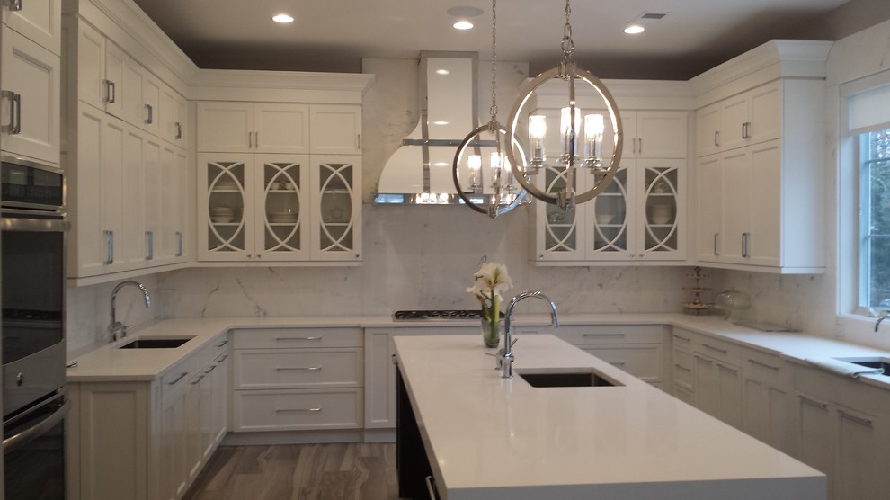 Large transitional u-shaped medium tone wood floor kitchen photo in New York with an undermount sink, shaker cabinets, white cabinets, white backsplash, stone slab backsplash, stainless steel appliances and an island