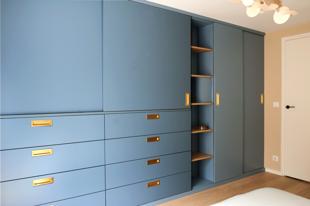 Photo of a mid-sized contemporary gender-neutral walk-in wardrobe in Other with beaded inset cabinets, blue cabinets, light hardwood floors and beige floor.