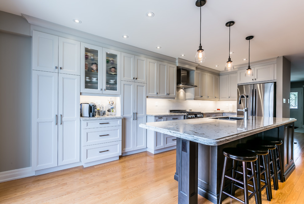 Inspiration for a mid-sized transitional l-shaped brown floor and light wood floor kitchen remodel in Toronto with a double-bowl sink, white cabinets, white backsplash, stainless steel appliances and an island