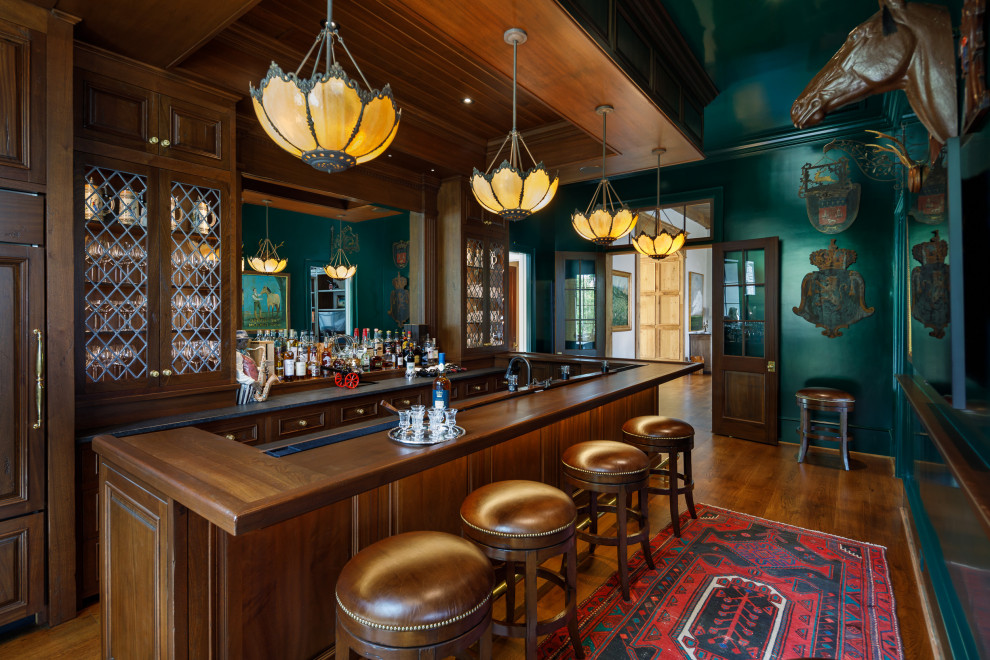 This is an example of a large traditional u-shaped seated home bar in Other with recessed-panel cabinets, medium wood cabinets, wood benchtops, medium hardwood floors, brown floor and brown benchtop.