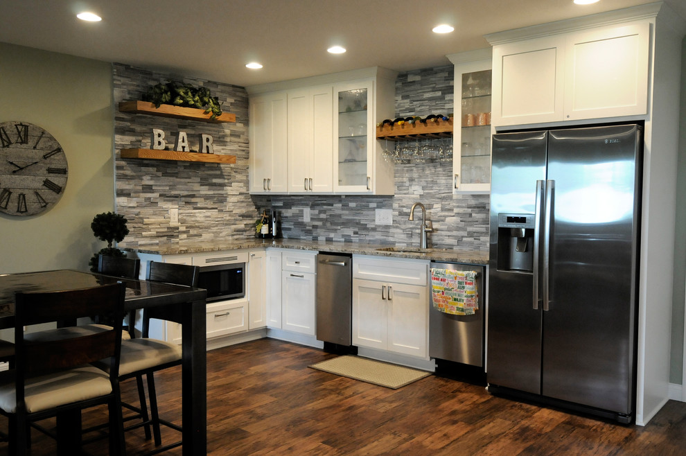 This is an example of a large tropical l-shaped wet bar in Minneapolis with an undermount sink, shaker cabinets, white cabinets, granite benchtops, grey splashback, stone tile splashback, limestone floors, brown floor and multi-coloured benchtop.