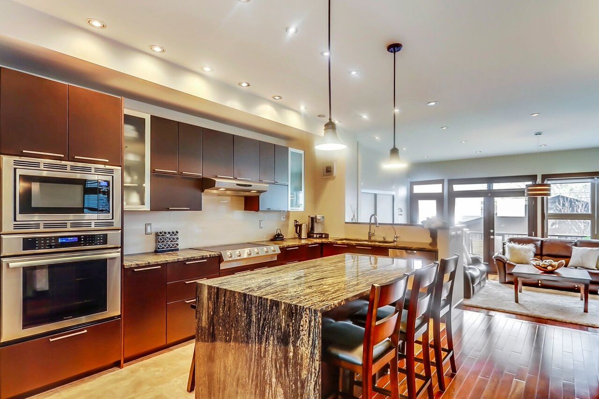 Open concept kitchen - large transitional l-shaped travertine floor open concept kitchen idea in Calgary with a double-bowl sink, flat-panel cabinets, dark wood cabinets, granite countertops, beige backsplash, stainless steel appliances and an island