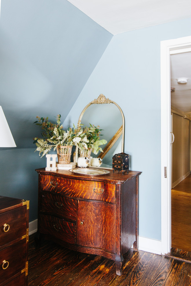 Idée de décoration pour une grande chambre parentale tradition avec un mur bleu, un sol en bois brun, une cheminée standard, un manteau de cheminée en plâtre, un sol marron et poutres apparentes.