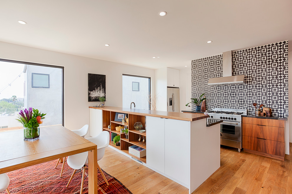 This is an example of a mid-sized scandinavian single-wall eat-in kitchen in Stockholm with flat-panel cabinets, medium wood cabinets, wood benchtops, multi-coloured splashback, stainless steel appliances, light hardwood floors and a peninsula.