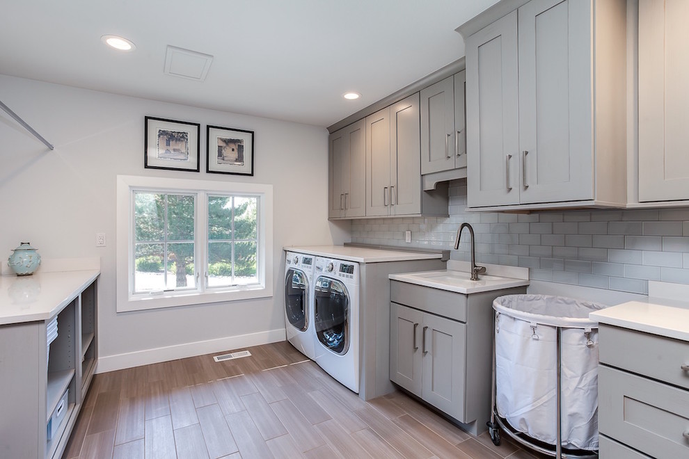 Photo of a large contemporary galley laundry room in Denver with an undermount sink, shaker cabinets, grey cabinets, quartz benchtops, grey walls, porcelain floors and a side-by-side washer and dryer.