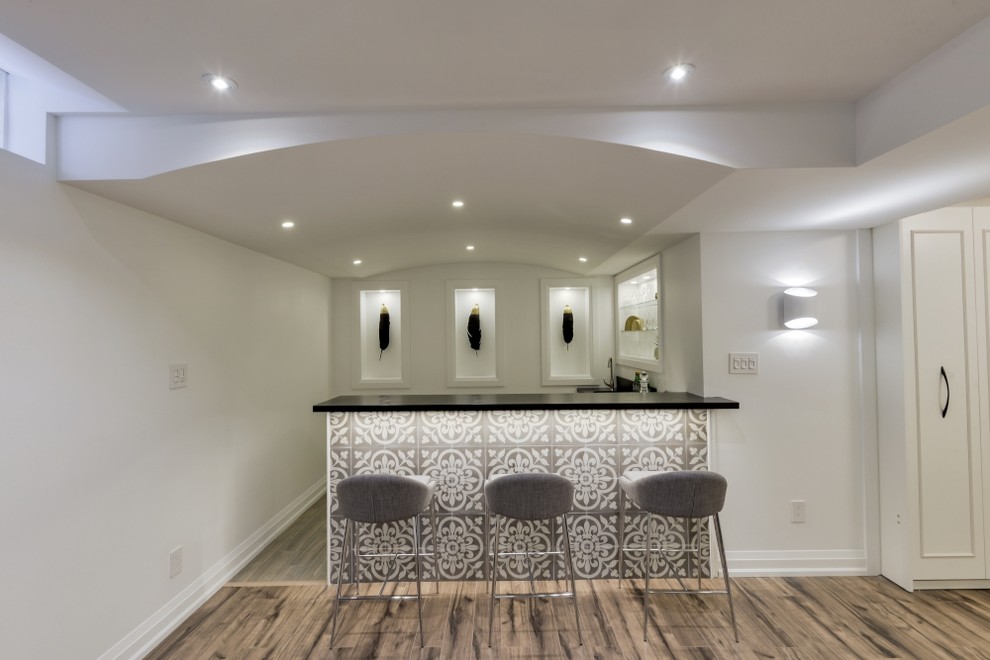 This is an example of a large contemporary l-shaped wet bar in Toronto with a drop-in sink, flat-panel cabinets, white cabinets, wood benchtops, black splashback, timber splashback, porcelain floors and grey floor.