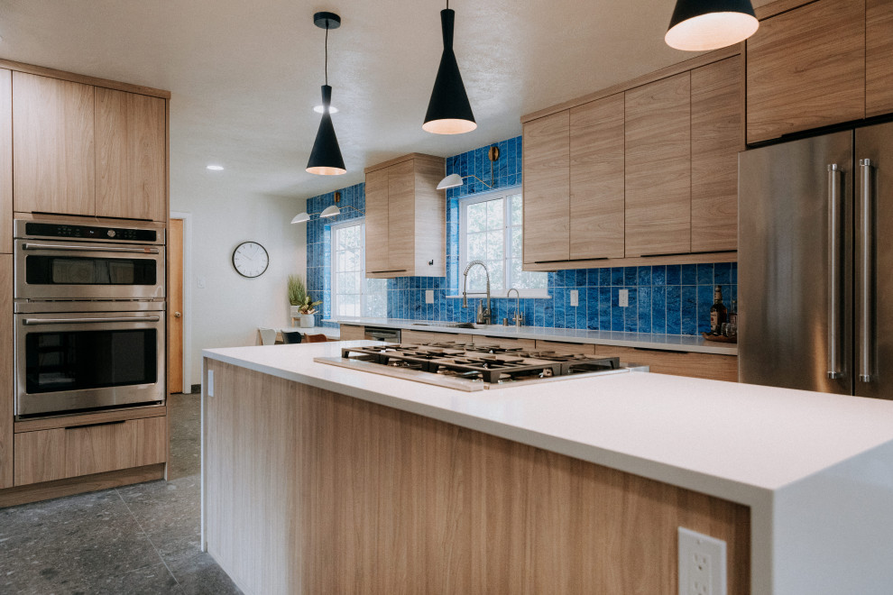Idee per una grande cucina moderna con lavello a vasca singola, ante lisce, ante in legno chiaro, paraspruzzi blu, elettrodomestici in acciaio inossidabile, pavimento grigio e top bianco