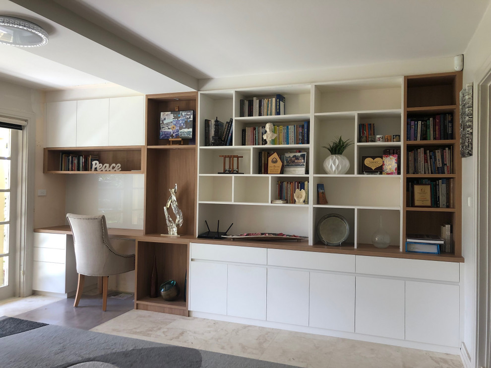This is an example of a large contemporary home office in Sydney with a library, white walls, travertine floors, a built-in desk and beige floor.