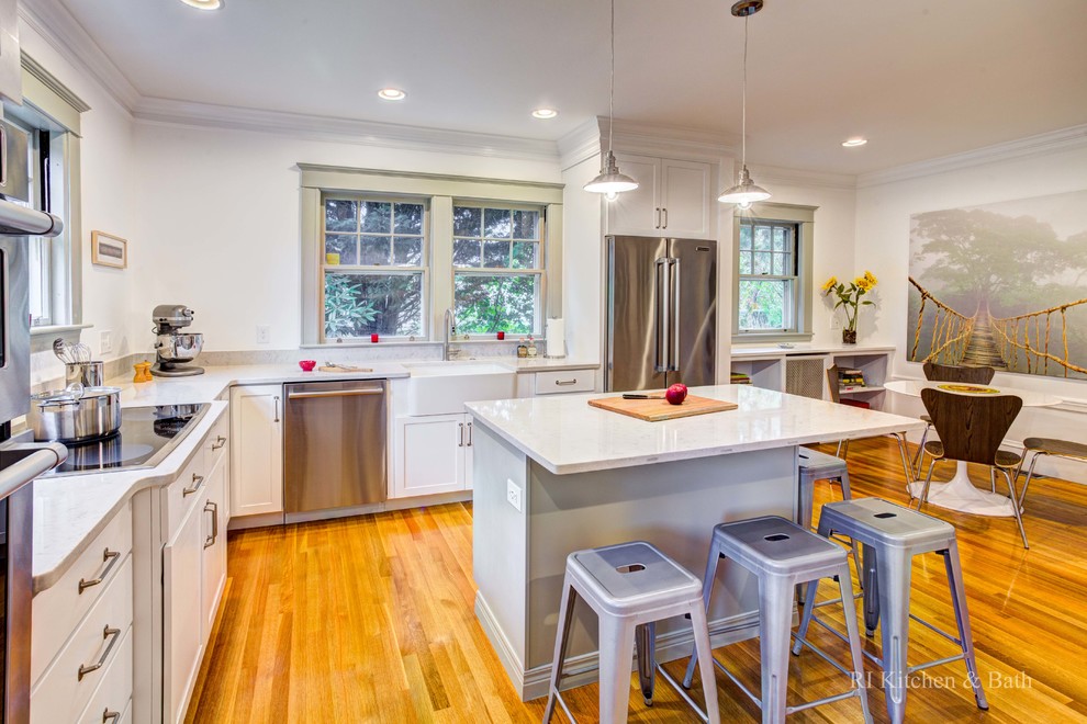 Photo of an expansive traditional l-shaped kitchen/diner in Providence with a belfast sink, shaker cabinets, white cabinets, engineered stone countertops, white splashback, stainless steel appliances, medium hardwood flooring and an island.