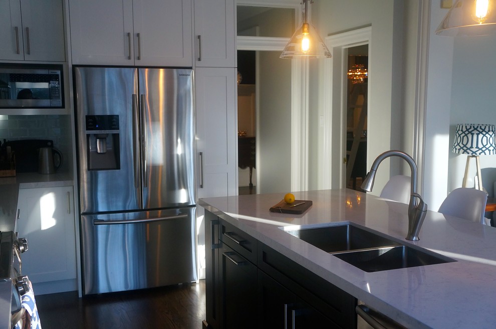 Transitional galley dark wood floor kitchen photo in Toronto with an undermount sink, shaker cabinets, white cabinets, quartz countertops, blue backsplash, glass tile backsplash, stainless steel appliances and an island