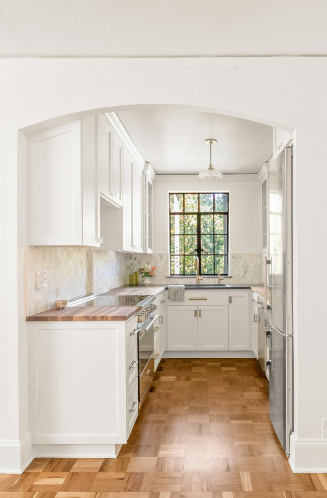 Inspiration for a small traditional galley separate kitchen in Portland with an undermount sink, shaker cabinets, wood benchtops, marble splashback, stainless steel appliances, light hardwood floors and black benchtop.