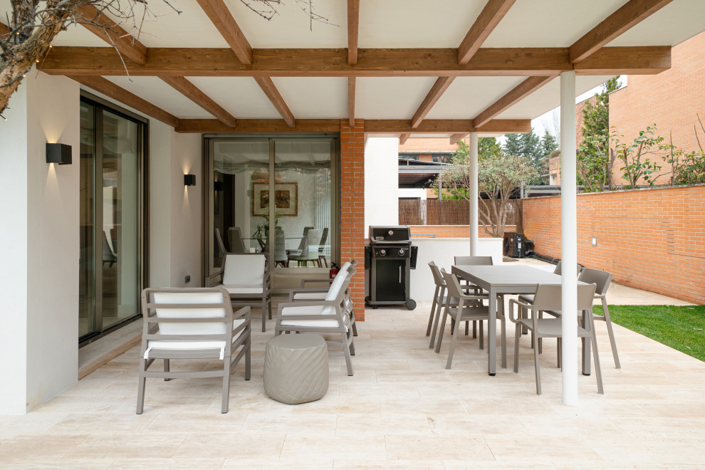 Photo of a large modern backyard verandah in Madrid with with columns, natural stone pavers, a roof extension and glass railing.