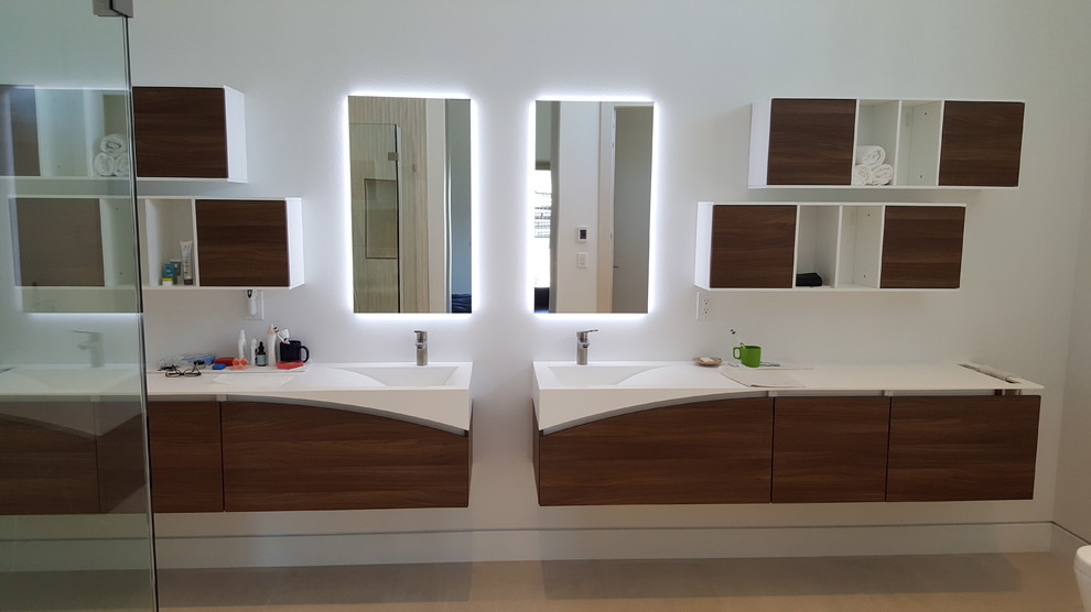 Photo of a large contemporary master bathroom in San Francisco with flat-panel cabinets, medium wood cabinets, a freestanding tub, white walls, porcelain floors, an integrated sink, solid surface benchtops and beige floor.