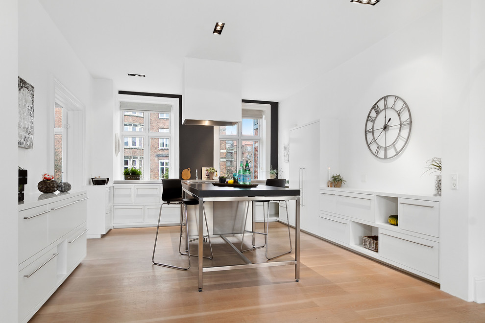 Photo of a scandinavian u-shaped eat-in kitchen in Copenhagen with flat-panel cabinets, white cabinets, light hardwood floors, with island, panelled appliances, beige floor and black benchtop.
