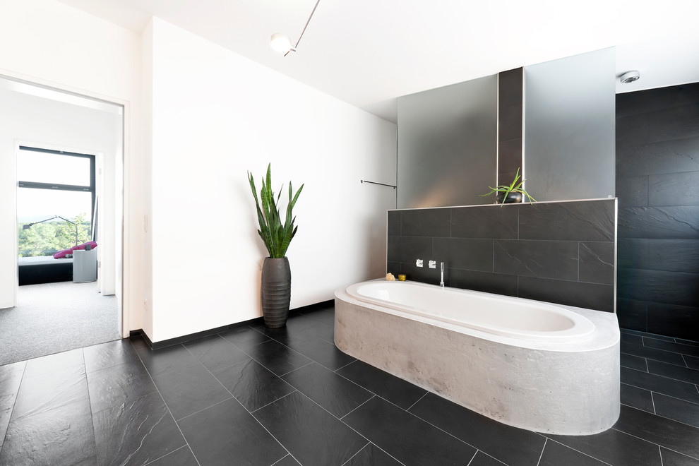 Inspiration for a large contemporary bathroom in Nuremberg with black tile, white walls, a drop-in tub, stone slab and slate floors.