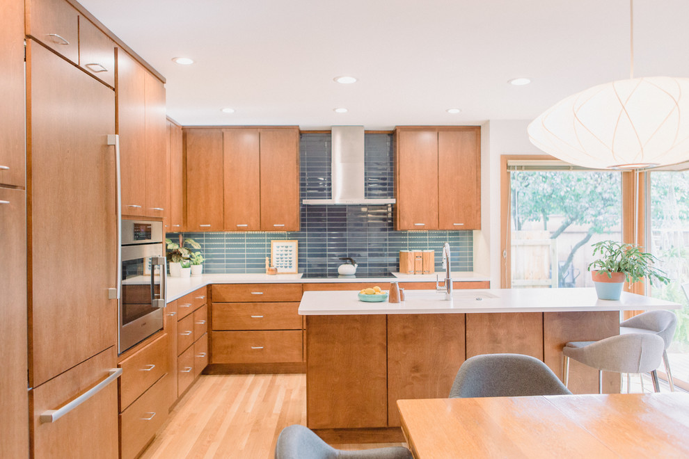 Mid-sized midcentury l-shaped eat-in kitchen in Grand Rapids with an undermount sink, flat-panel cabinets, medium wood cabinets, quartz benchtops, blue splashback, panelled appliances, light hardwood floors, with island and white benchtop.
