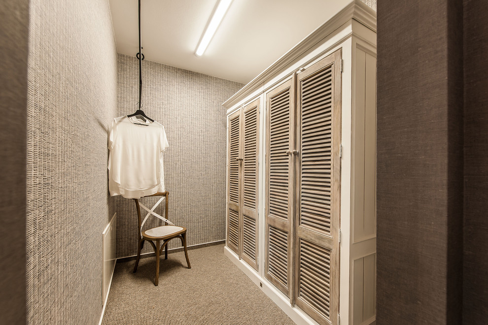 Photo of a small beach style gender-neutral dressing room with light wood cabinets, carpet, beige floor and louvered cabinets.