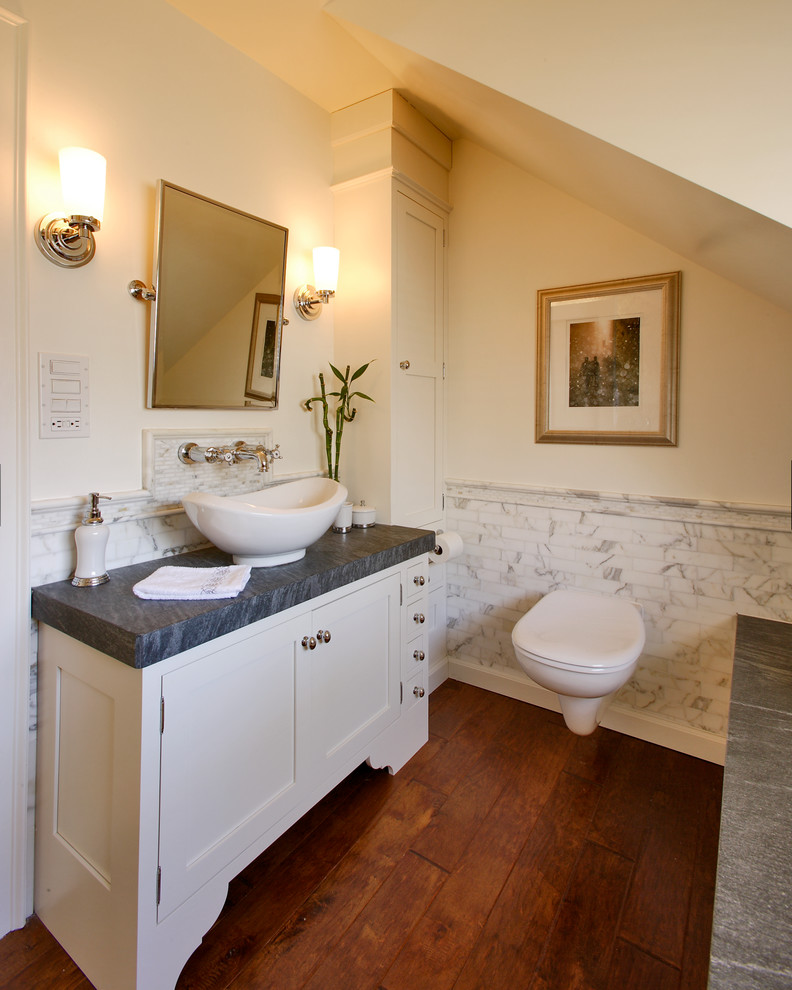 Mid-sized transitional master bathroom in New York with a vessel sink, shaker cabinets, white cabinets, a wall-mount toilet, white tile, beige walls, medium hardwood floors, an alcove shower, subway tile, soapstone benchtops, brown floor and a hinged shower door.