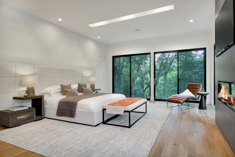 Photo of a large modern master bedroom in New York with white walls, light hardwood floors and a hanging fireplace.
