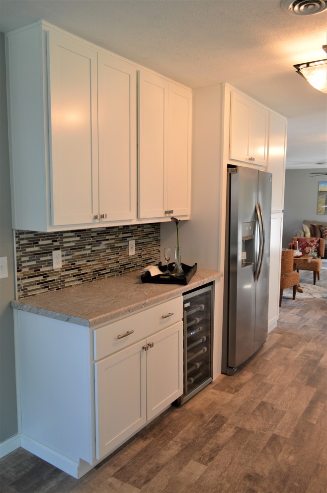 This is an example of a mid-sized contemporary galley open plan kitchen in Indianapolis with an undermount sink, shaker cabinets, white cabinets, laminate benchtops, multi-coloured splashback, matchstick tile splashback, stainless steel appliances, no island, brown floor and grey benchtop.