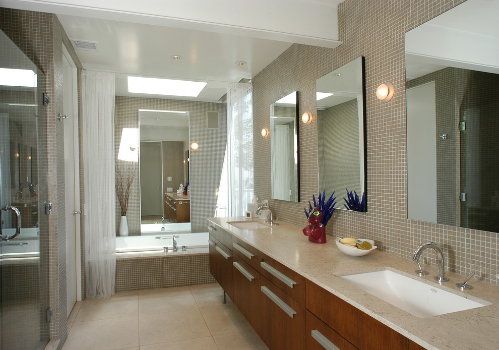 Large midcentury master bathroom in Los Angeles with an undermount sink, flat-panel cabinets, dark wood cabinets, limestone benchtops, a drop-in tub, a one-piece toilet, beige tile, beige walls, limestone floors, a double shower and glass tile.