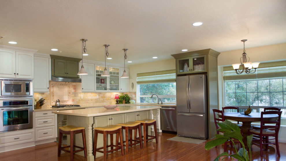 Open concept kitchen - mid-sized transitional l-shaped medium tone wood floor open concept kitchen idea with a double-bowl sink, raised-panel cabinets, white cabinets, white backsplash, stainless steel appliances and an island