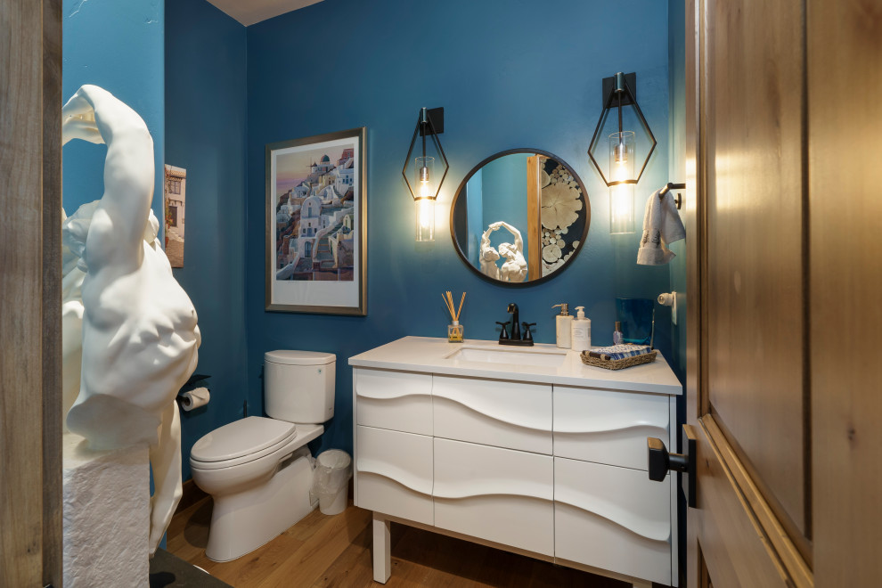Photo of a small contemporary powder room in Denver with white cabinets, a two-piece toilet, an undermount sink, engineered quartz benchtops, white benchtops, a freestanding vanity, blue walls, medium hardwood floors and brown floor.