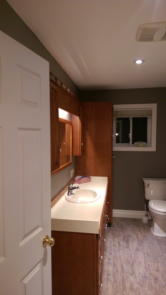Example of a mid-sized transitional master vinyl floor and multicolored floor alcove bathtub design with recessed-panel cabinets, medium tone wood cabinets, a two-piece toilet, gray walls, laminate countertops and yellow countertops