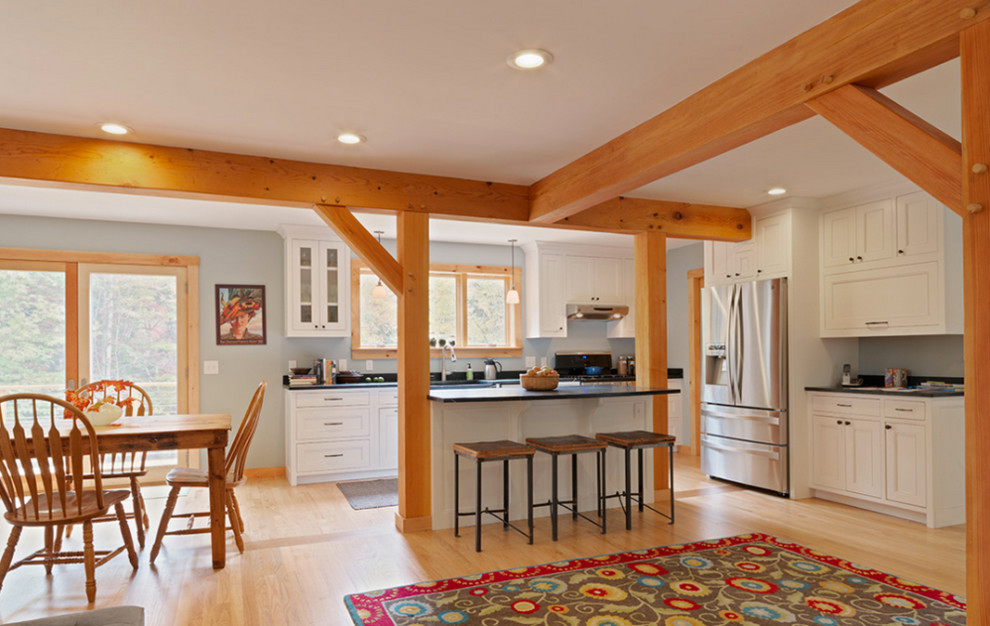 Inspiration for a mid-sized country l-shaped open plan kitchen in Burlington with beaded inset cabinets, white cabinets, soapstone benchtops, stainless steel appliances, light hardwood floors, with island and beige floor.