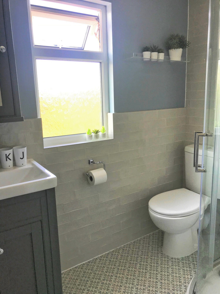 Idée de décoration pour une petite salle de bain principale design avec des portes de placard grises, une douche d'angle, WC à poser, un carrelage beige, des carreaux de porcelaine, un mur bleu, un sol en carrelage de porcelaine, un sol bleu, une cabine de douche à porte coulissante, meuble simple vasque et meuble-lavabo sur pied.