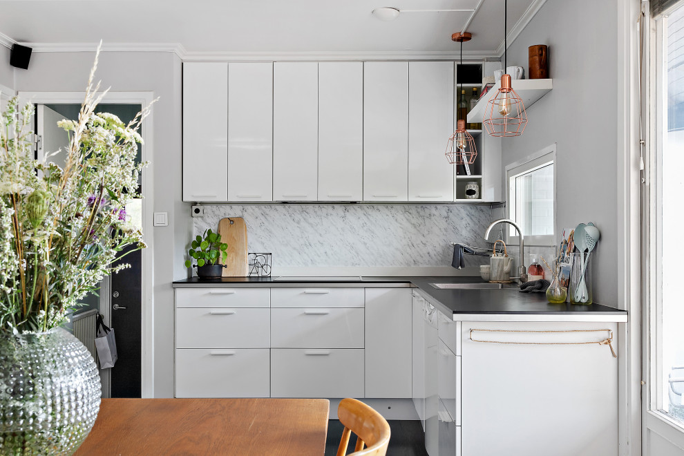 This is an example of a small contemporary l-shaped eat-in kitchen in Other with a drop-in sink, flat-panel cabinets, white cabinets, grey splashback, no island, black floor and black benchtop.