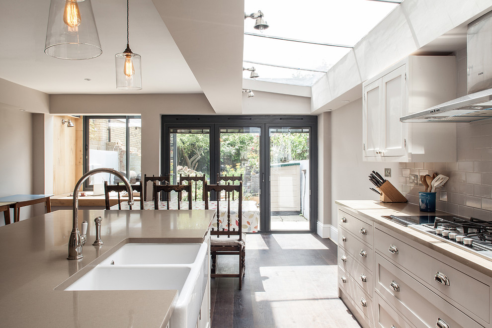 Inspiration for a transitional eat-in kitchen in London with a farmhouse sink, shaker cabinets, beige cabinets, granite benchtops, subway tile splashback, dark hardwood floors, with island and beige splashback.