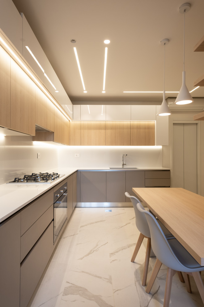 Large modern l-shaped kitchen in London with grey cabinets, white splashback, stone slab splashback, stainless steel appliances, marble floors, a peninsula, white benchtop and recessed.
