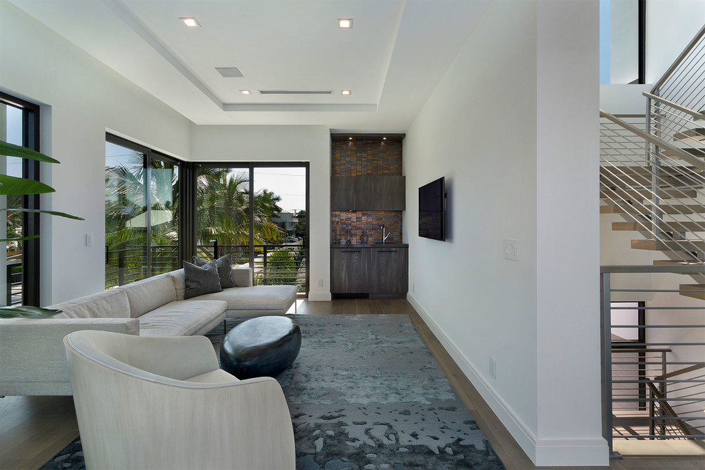 This is an example of a mid-sized modern open concept family room in Miami with beige walls, light hardwood floors, a standard fireplace, a concrete fireplace surround, a built-in media wall and beige floor.