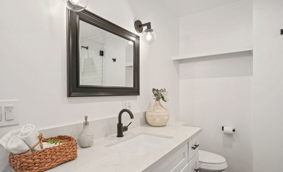 This is an example of a contemporary bathroom in Los Angeles with shaker cabinets, white cabinets, a one-piece toilet, white walls, medium hardwood floors, an undermount sink, solid surface benchtops, brown floor, white benchtops, an enclosed toilet, a single vanity and a built-in vanity.