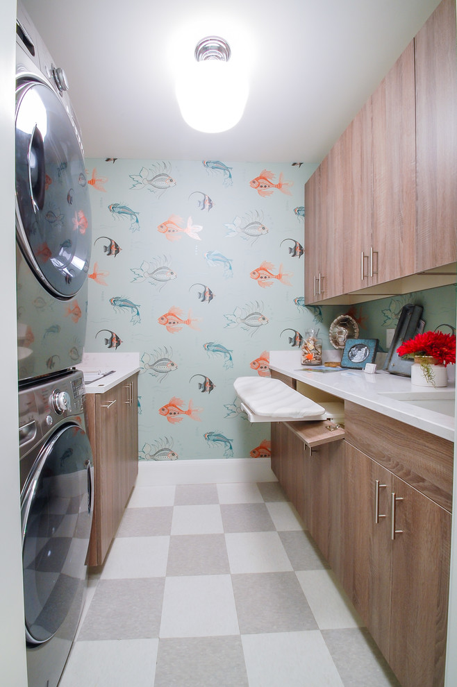 This is an example of a mid-sized beach style galley dedicated laundry room in Minneapolis with an undermount sink, flat-panel cabinets, marble benchtops, blue walls, linoleum floors, a stacked washer and dryer and medium wood cabinets.