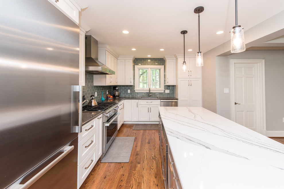 This is an example of a mid-sized transitional u-shaped open plan kitchen in DC Metro with an undermount sink, recessed-panel cabinets, white cabinets, granite benchtops, green splashback, subway tile splashback, stainless steel appliances, medium hardwood floors, with island, brown floor and white benchtop.