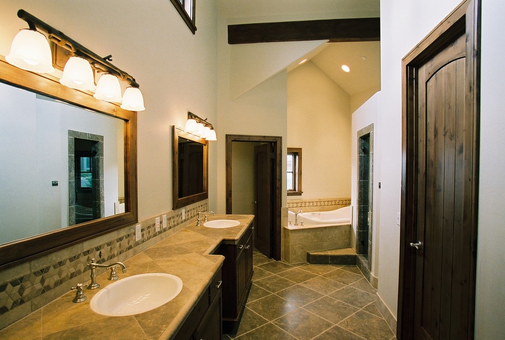 This is an example of a large country master bathroom in Salt Lake City with recessed-panel cabinets, dark wood cabinets, a drop-in tub, an alcove shower, beige tile, gray tile, porcelain tile, white walls, porcelain floors, a drop-in sink, tile benchtops, grey floor, a hinged shower door and beige benchtops.