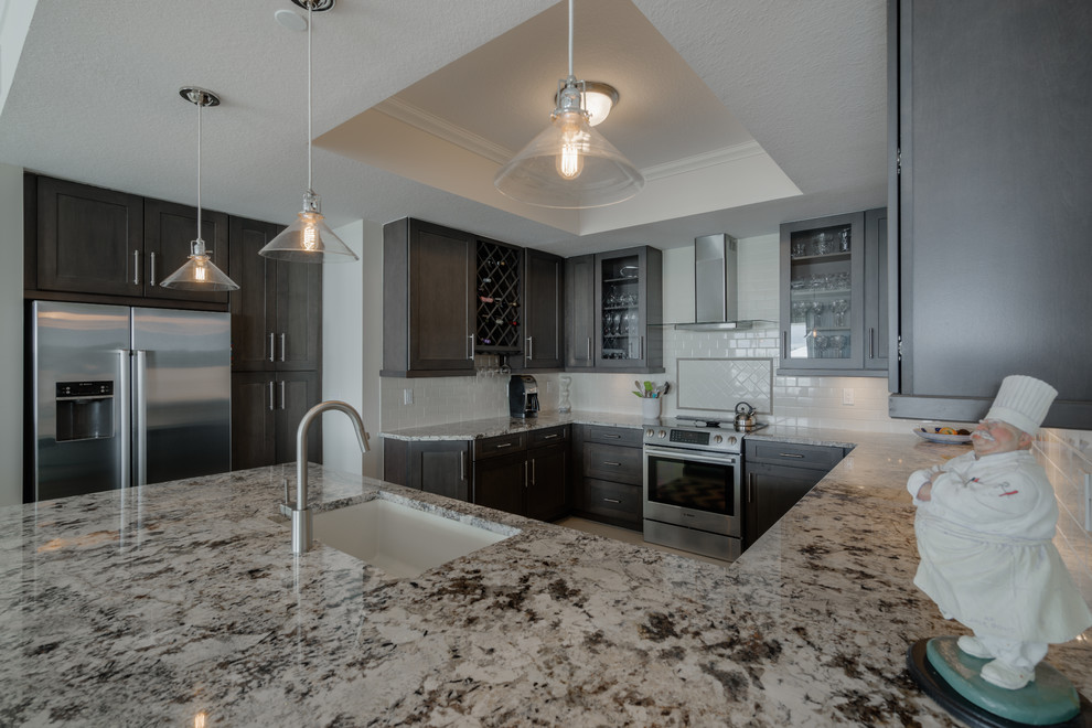 This is an example of a large beach style u-shaped open plan kitchen in Miami with an undermount sink, recessed-panel cabinets, dark wood cabinets, granite benchtops, white splashback, ceramic splashback, stainless steel appliances, ceramic floors and a peninsula.